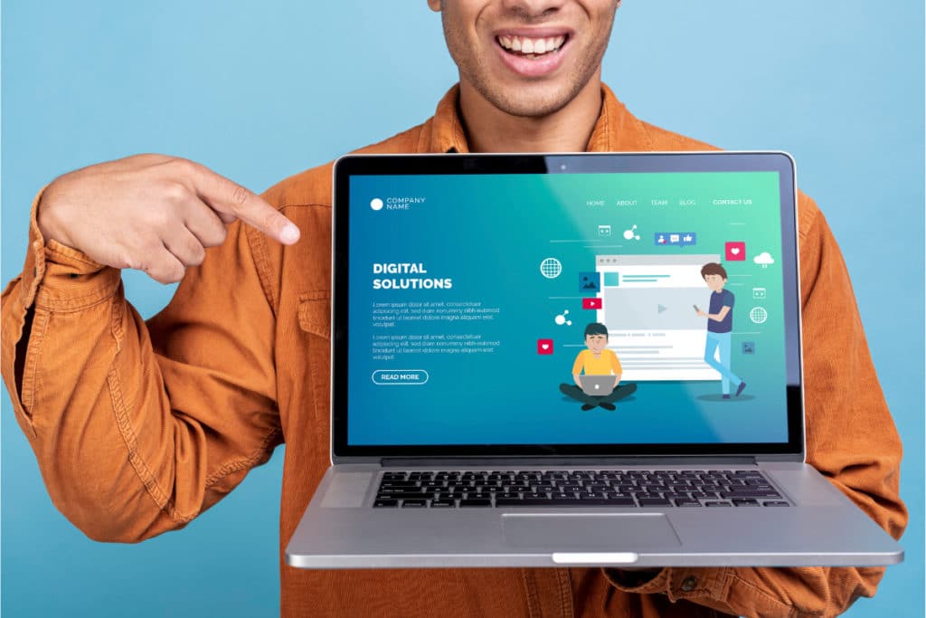 un homme en chemise orange pointe l'écran d'un macbook pro sur lequel il y a un template d'une page d'un site web d'une entreprise.