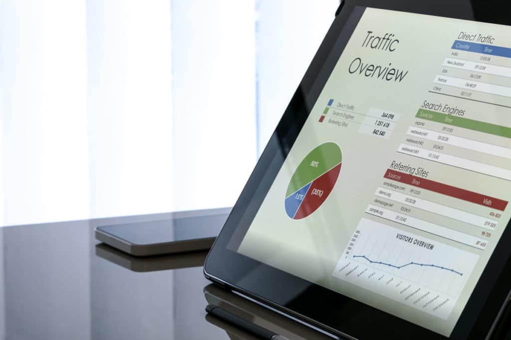 une tablette est posée sur un bureau. elle affiche des données et un graphique avec comme titre "Traffic Overview". Un téléphone portable est posé à côté de la tablette.
