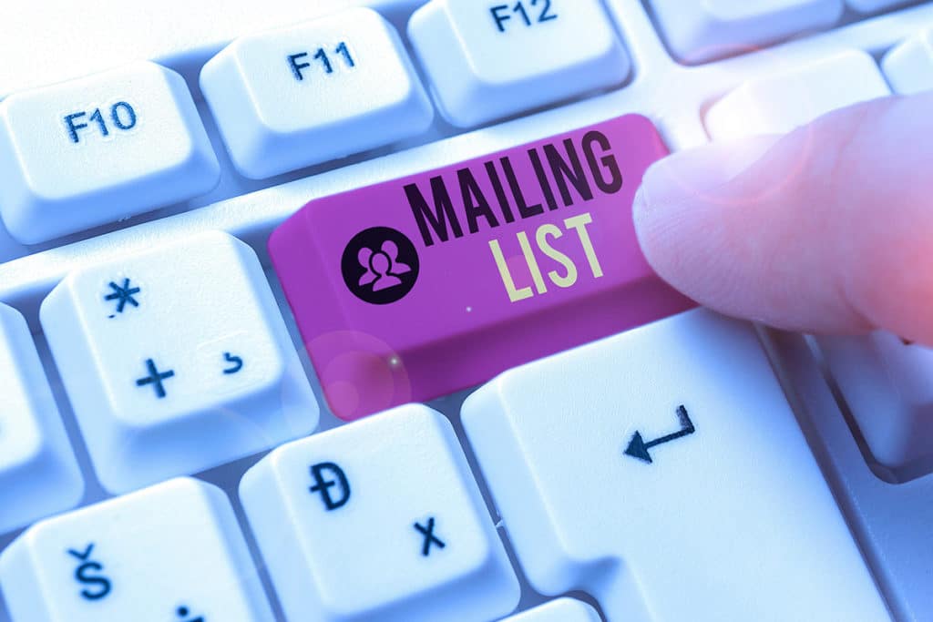 Un main qui clic sur un bouton "mailing list" sur un clavier d'ordinateur.