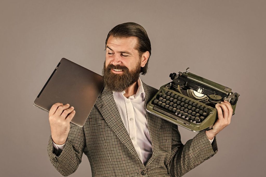 Un rédacteur web qui tient unordinateur portable d'une main et une machine à écrire ancienne