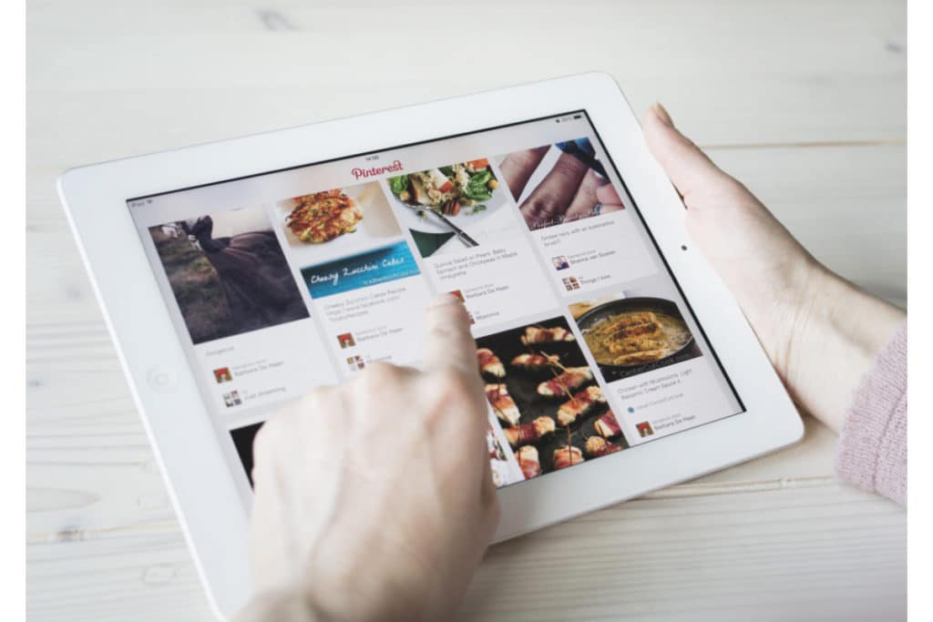 vue sur 2 mains qui tiennent une tablette apple blanche sur laquelle figure l'application Pinterest.