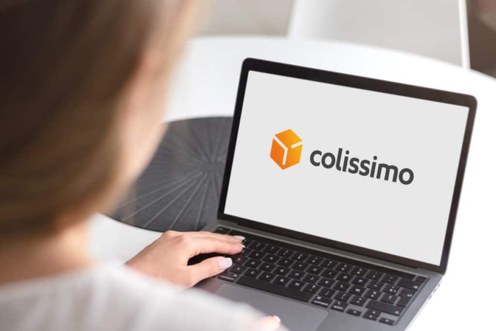 une femme a la main posée sur un ordinateur portable sur lequel est à affiché le logo de Colissimo en plein écran.