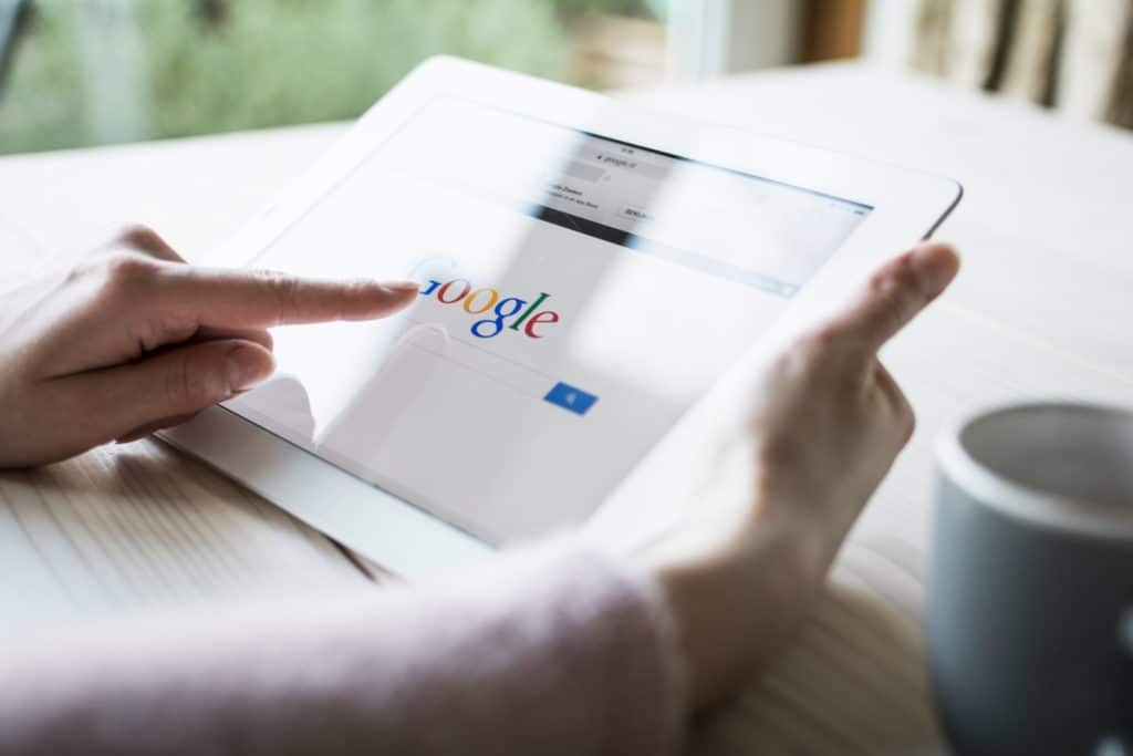 vue sur deux mains qui tiennent une tablette sur laquelle est affichée la page de recherche de Google.