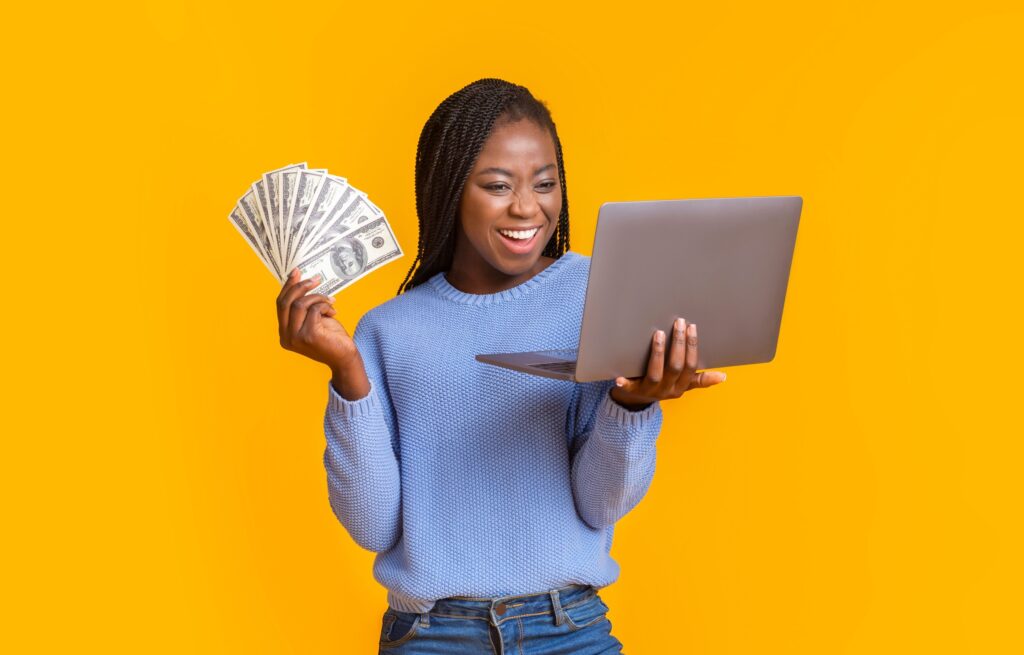 jeune femme en pull bleu souriante qui tient un ordinateur et des billets, comment se faire rembourser sur Aliexpress.