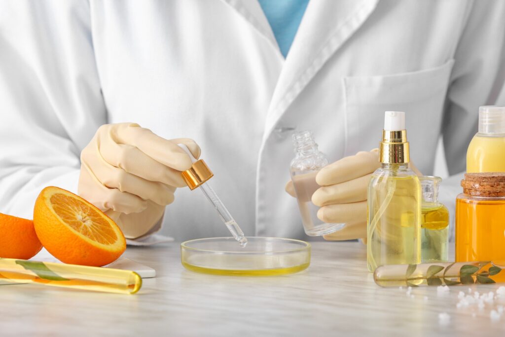 Gros plan sur des mains préparant un produit cosmétique naturel à base d'orange en laboratoire. Des flacons et des tranches d'orange sont posés sur la table de laboratoire.