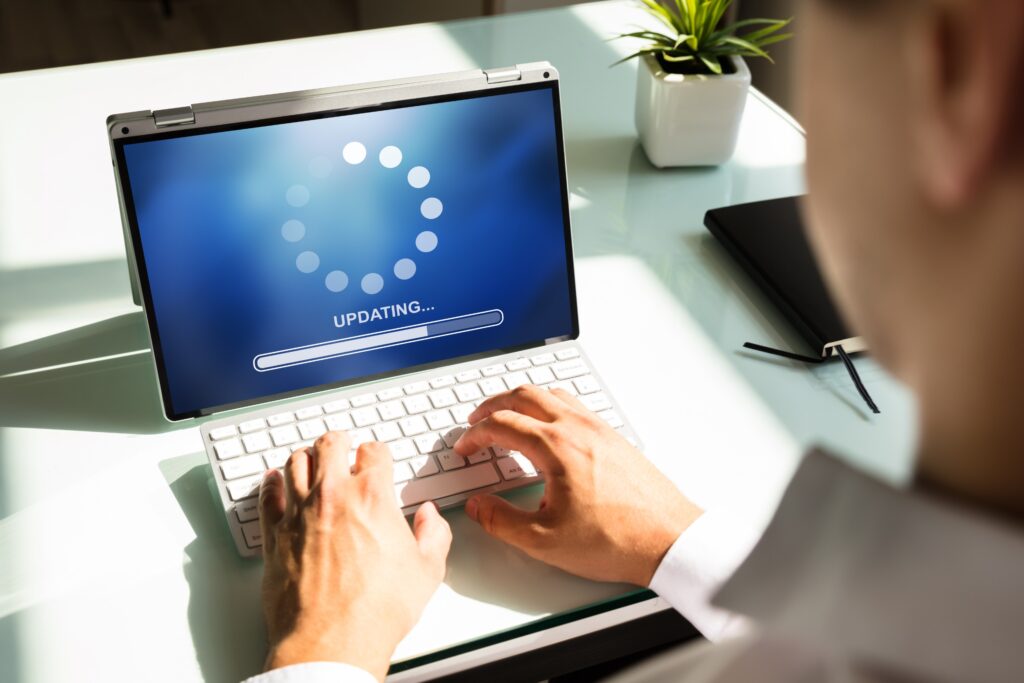 Les mains d'un homme placées sur le clavier d'un ordinateur portable dont l'écran affiche "uploading" pour exprimer le concept de mise à jour.