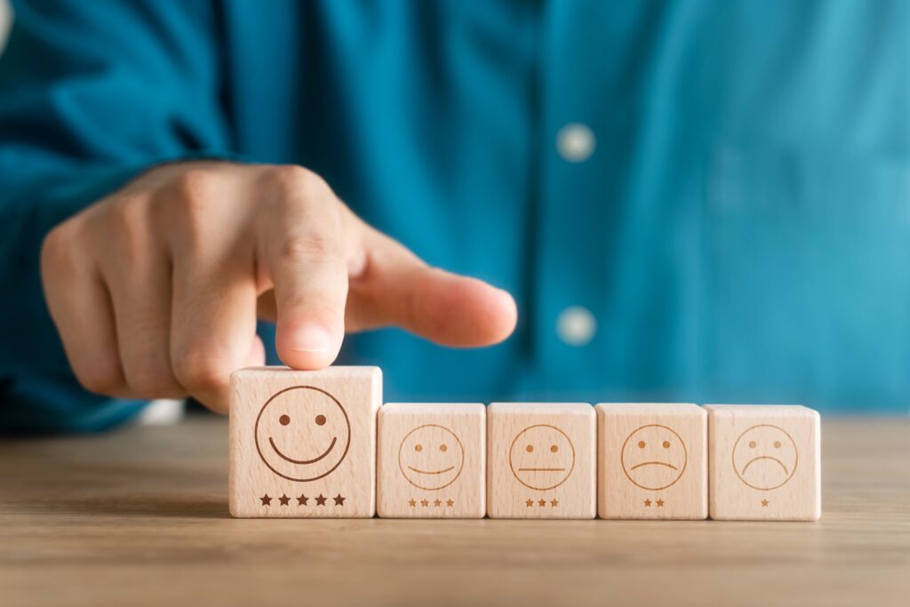 Le doigt d'un homme montrant un cube de bois avec un émoji souriant et 5 étoiles gravés dessus pour exprimer le concept de satisfaction des utilisateurs. Le cube de bois est aligné avec d'autres cubes.