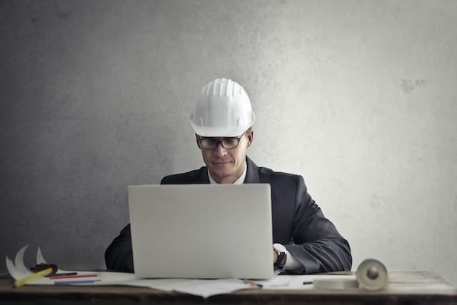 Un chef de chantier avec un casque sur la tête rédige du contenu sur son ordinateur à propos du travail en bâtiment grâce à son expérience du terrain