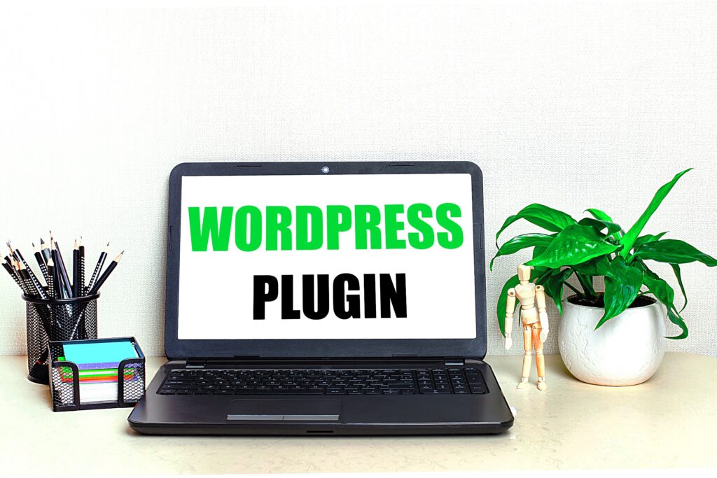 Un ordinateur portable sur l'écran duquel s'affiche le mot "Wordpress Plugin", posé sur un bureau à côté d'un pot de crayons et d'une vase de plante verte.