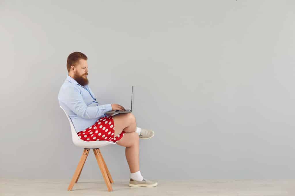 Un freelance Wordpress qui travail sur son ordinateur assis sur une chaise habillé d'une chemise et d'un caleçon rouge à pois blancs