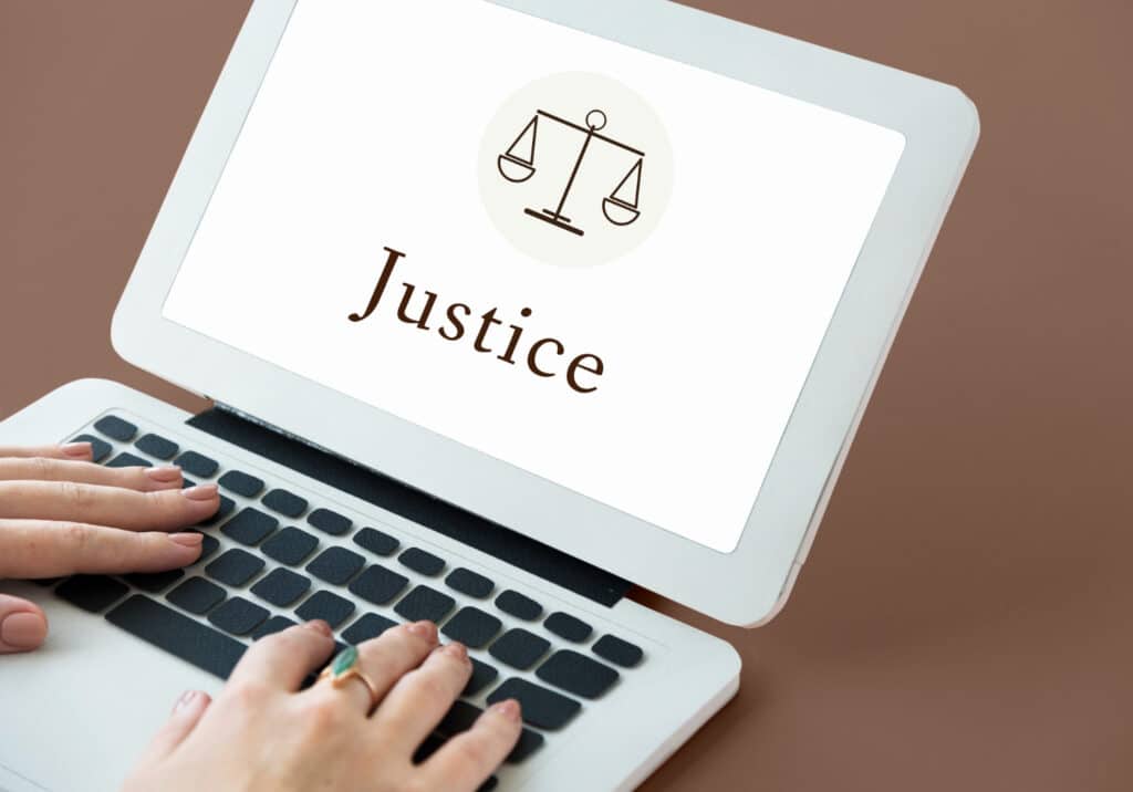 Une main posée sur le clavier d'un ordinateur portable avec le mot "Justice" sur l'écran.