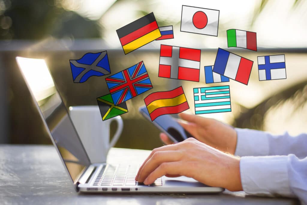 Une main sur le clavier d'un ordinateur portable d'où sortent différents drapeaux de différents pays.